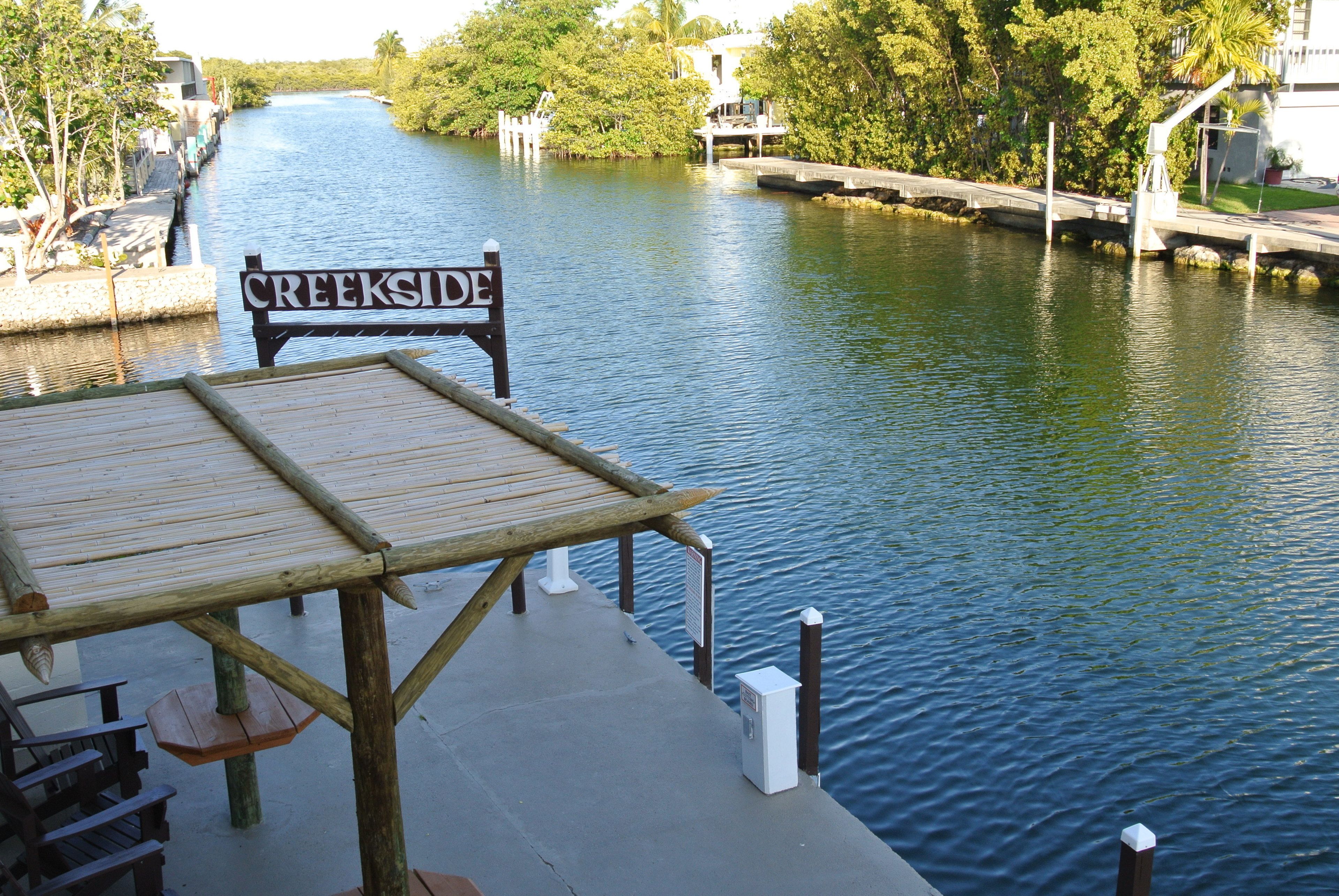 Un muelle de madera con un letrero que dice "Creekside" que da vista a un río tranquilo.