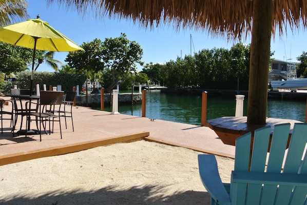 Un patio frente al agua con mesas al aire libre, una sombrilla amarilla y vistas al mar.