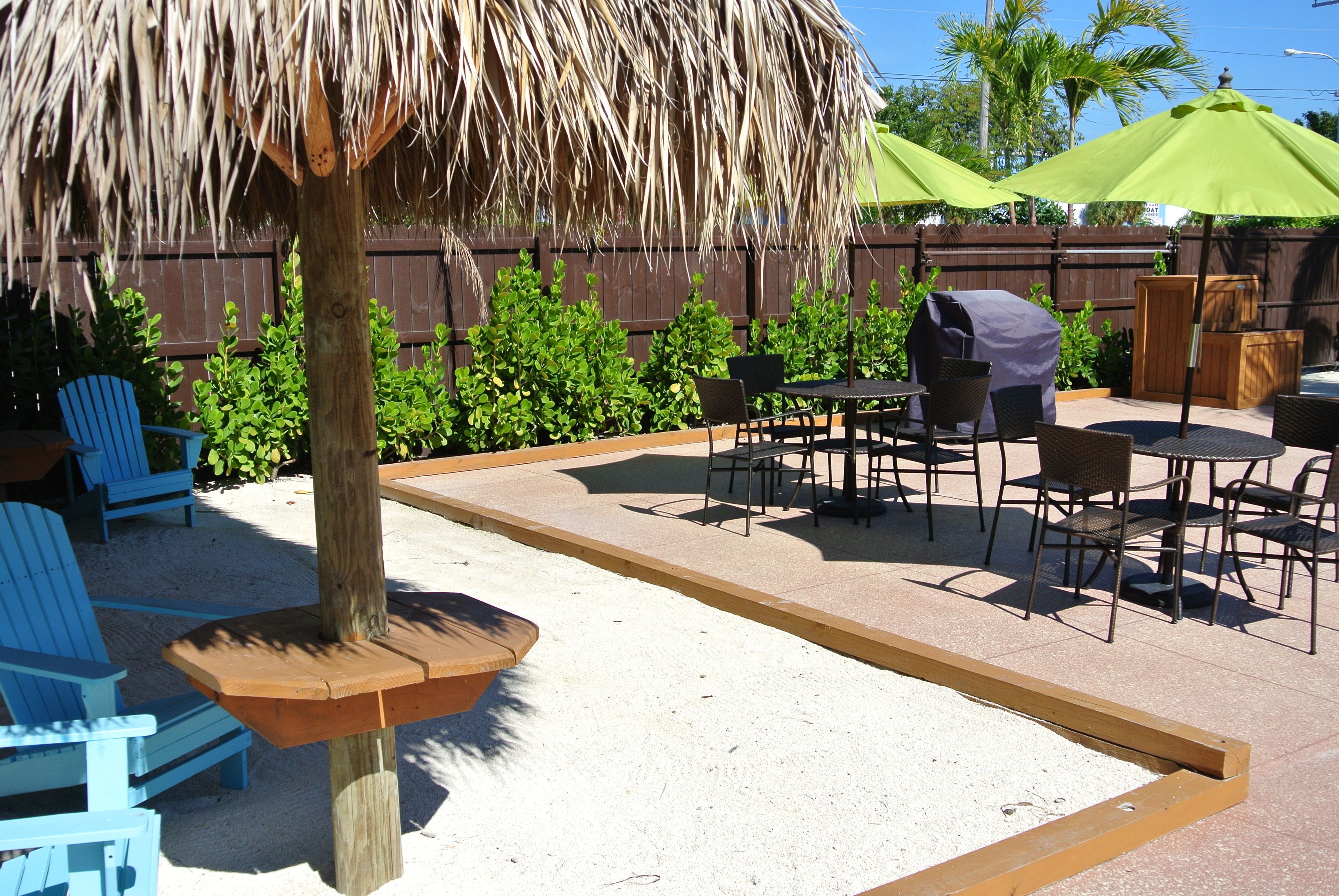 A patio area with blue chairs, a wooden table, a barbecue grill, and a thatched umbrella.