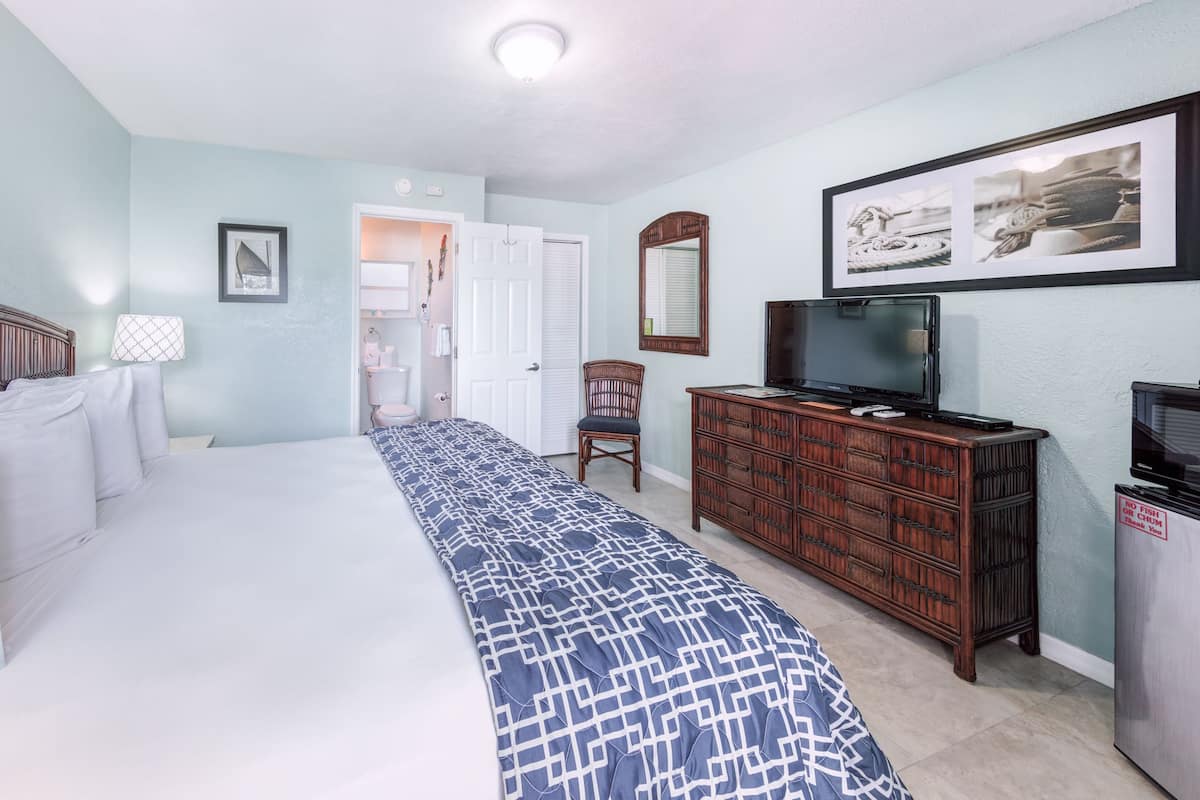 Une chambre d’hôtel avec un grand lit, une commode, un téléviseur et un tableau encadré au mur.