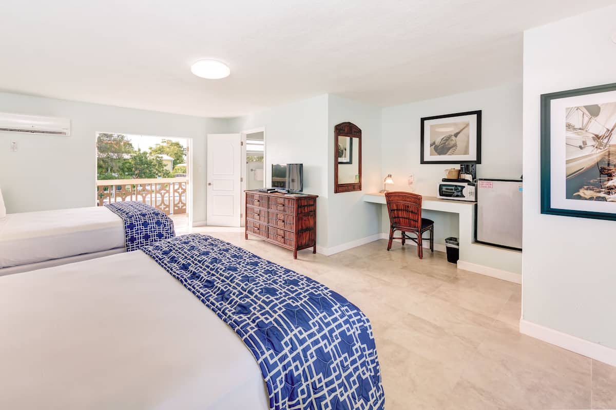 Une chambre d’hôtel avec deux lits, un bureau, une chaise, une commode et un balcon avec vue.