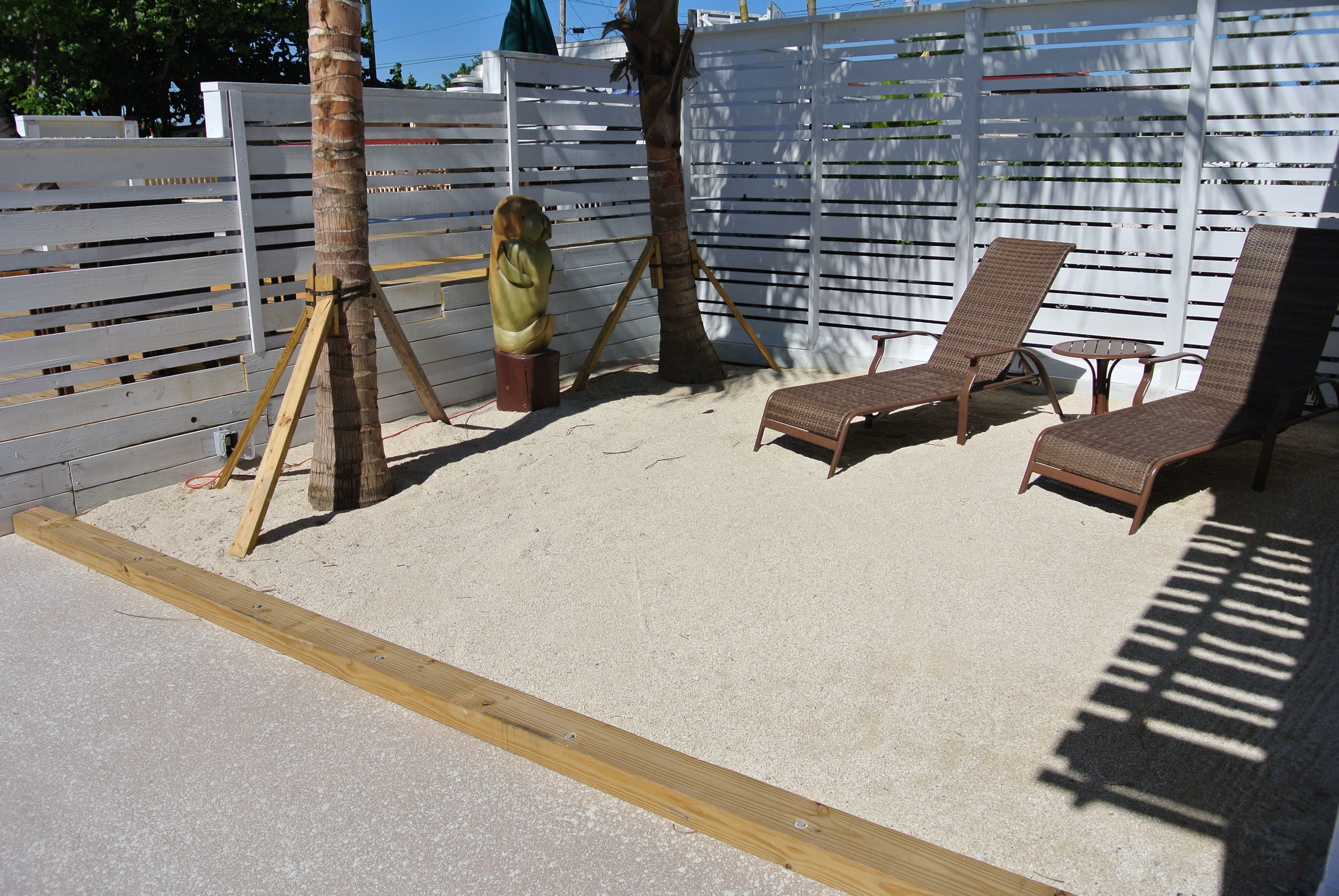 A sandy outdoor area with two lounge chairs and a wooden bench.