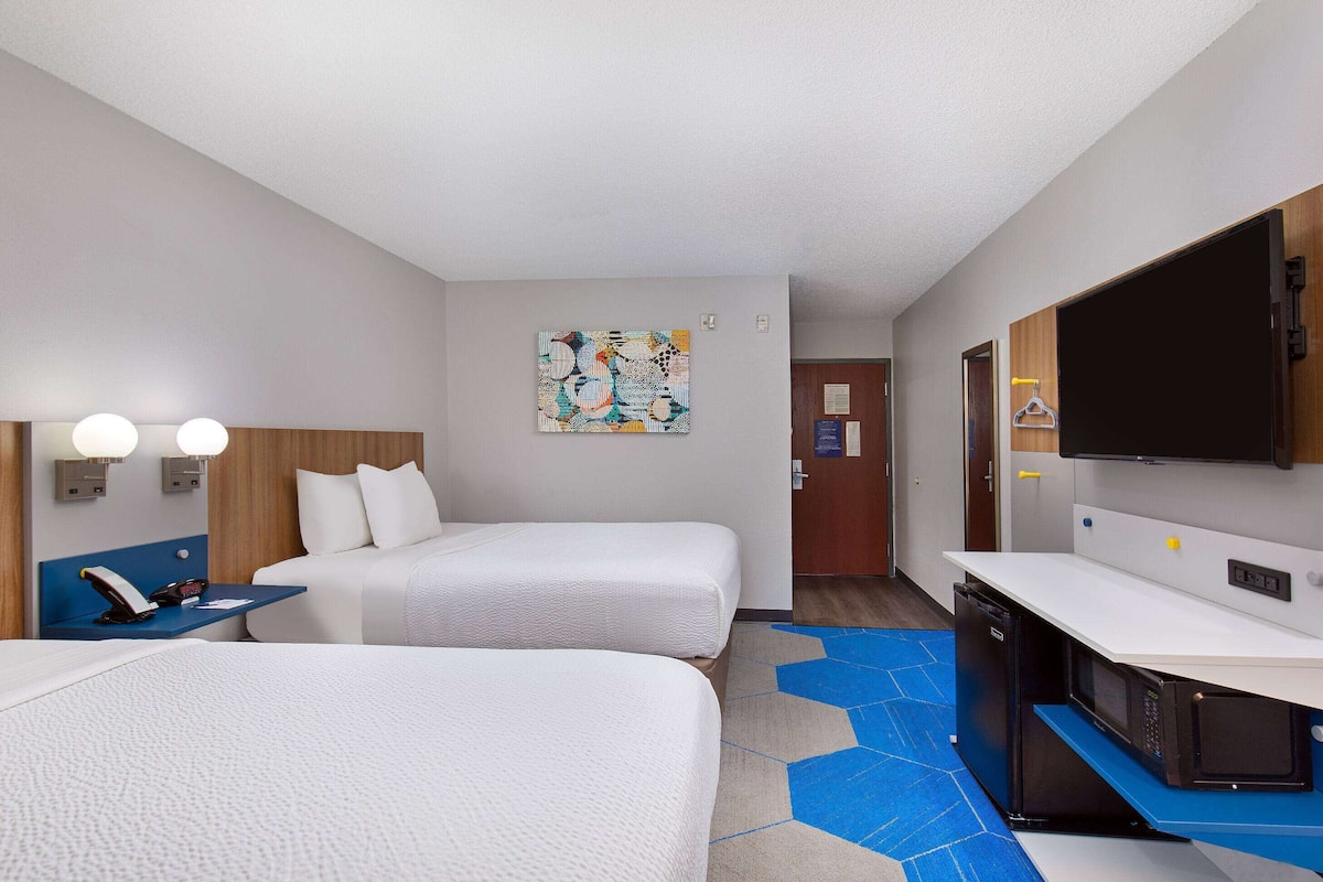 A hotel room with two beds, a desk with a phone, a microwave, and a TV on a cabinet.