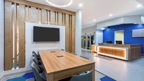 A modern hotel lobby with a wooden reception desk, a flat-screen TV mounted on the wall, and a conference room with a wooden table and chairs. - Microtel Inn and Suites by Wyndham Columbus North (Columbus)