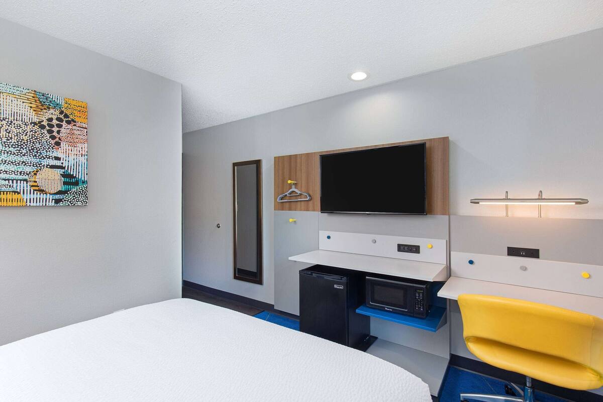 A modern hotel room with a bed, a desk with a computer, a TV, and a small fridge.