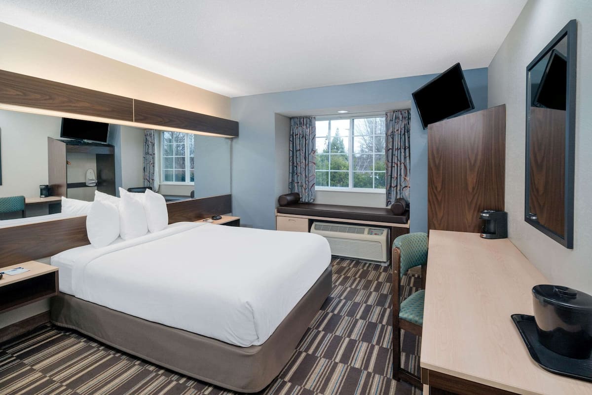 A hotel room with a large bed, a desk, a chair, a television, and a window with curtains.