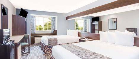 A hotel room with two beds, a desk, a TV, and a large window with curtains.