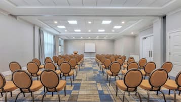 Un salón de conferencias con hileras de sillas, una pantalla para proyector y suelo alfombrado.
