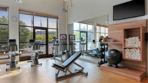 Un gimnasio con equipamiento de ejercicio, amplias ventanas y un mostrador de recepción de madera.