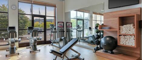 A gym with exercise equipment, large windows, and a wooden reception desk.