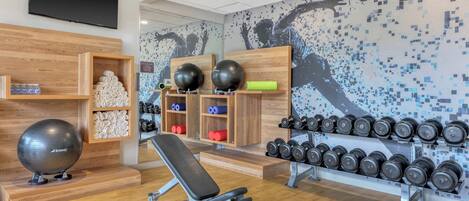 A gym with exercise equipment, wooden benches, and a wall-mounted TV.