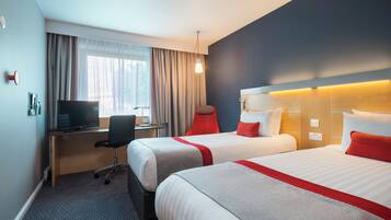 Habitación de hotel con dos camas, un escritorio con computadora, una silla y una ventana con cortinas.