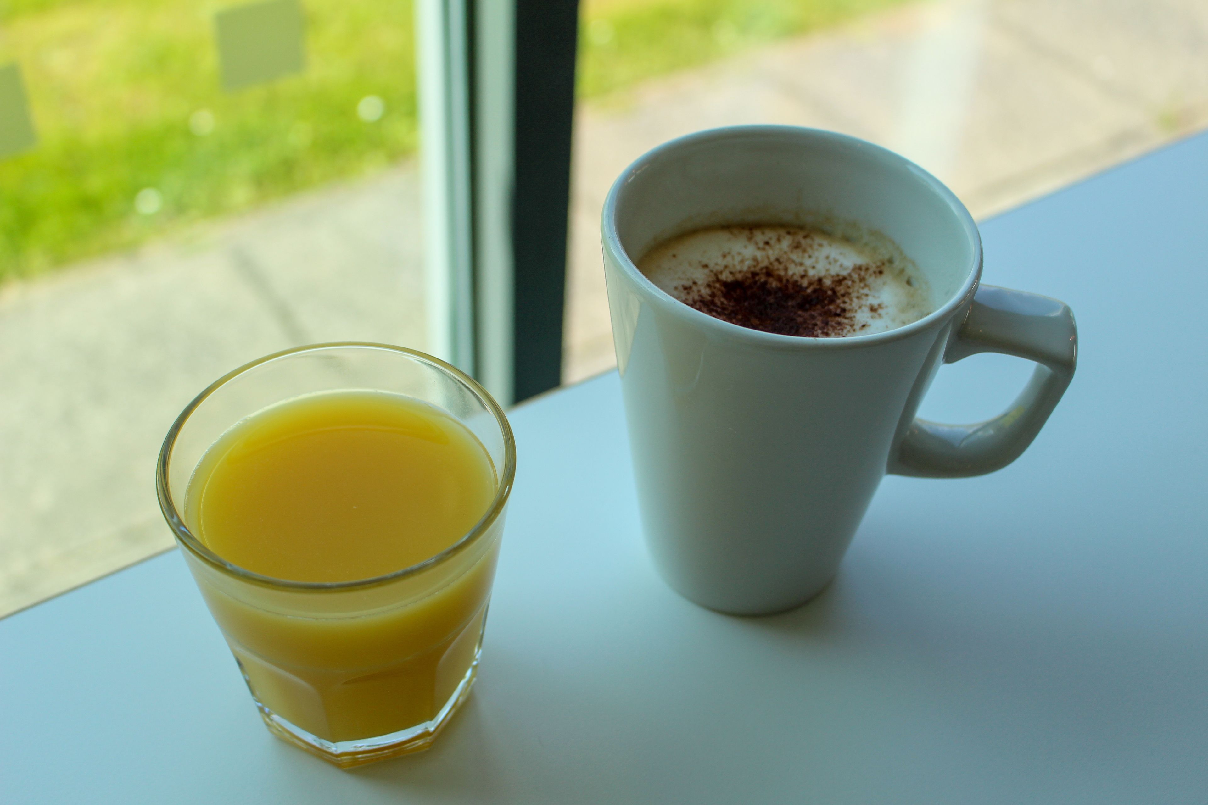 Ein Glas Orangensaft und eine weiße Tasse mit einem Getränk auf einem Tisch.