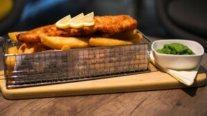 A tray of fish and chips with lemon slices and a small bowl of sauce.