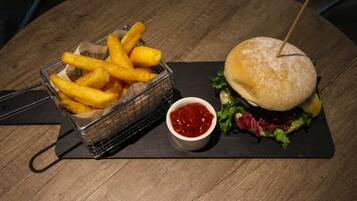 Un repas composé d’un hamburger piqué d’un cure-dent, d’un panier de frites et d’un petit bol de ketchup, le tout posé sur une table en bois.
