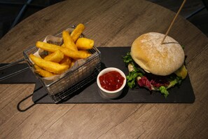 A meal consisting of a burger with a toothpick, a basket of fries, and a small bowl of ketchup on a wooden table.