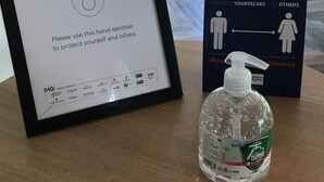 A framed sign emphasizing well-being and physical distancing, a hand sanitizer bottle, and a window view.