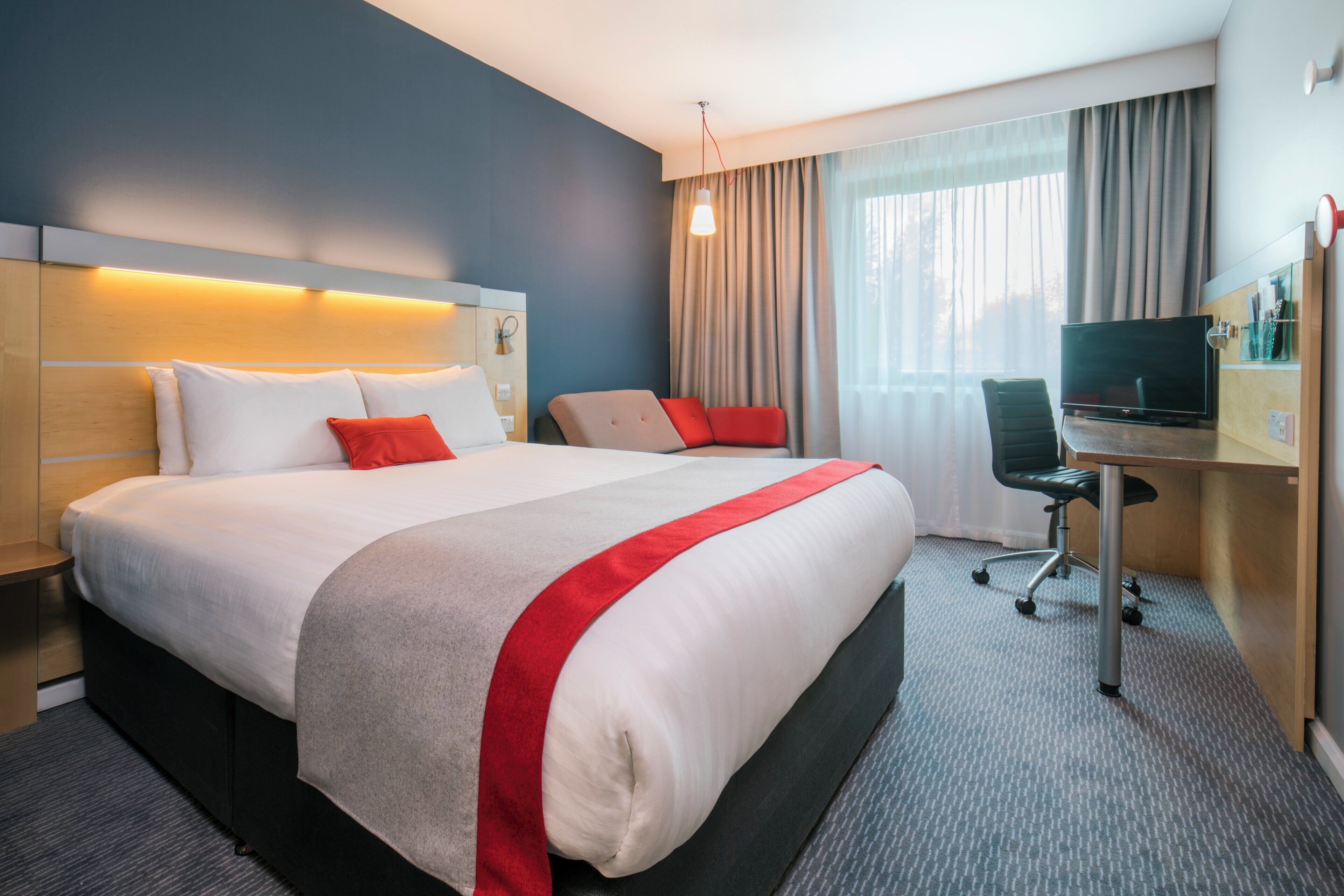Een hotelkamer met een groot bed, een bureau met stoel, een televisie en een raam met gordijnen.