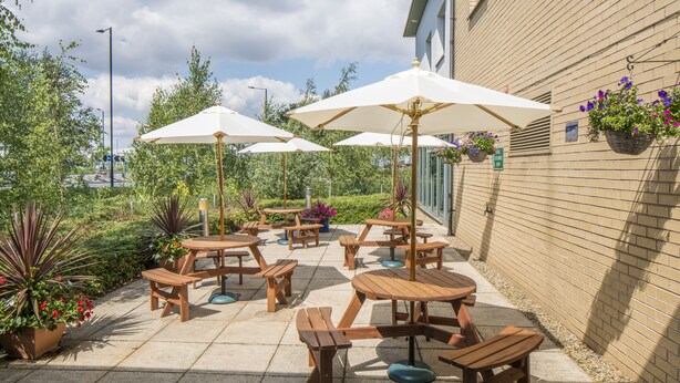 An outdoor patio with wooden tables and benches, white umbrellas, and potted plants. - Holiday Inn Express Doncaster by IHG (Doncaster)