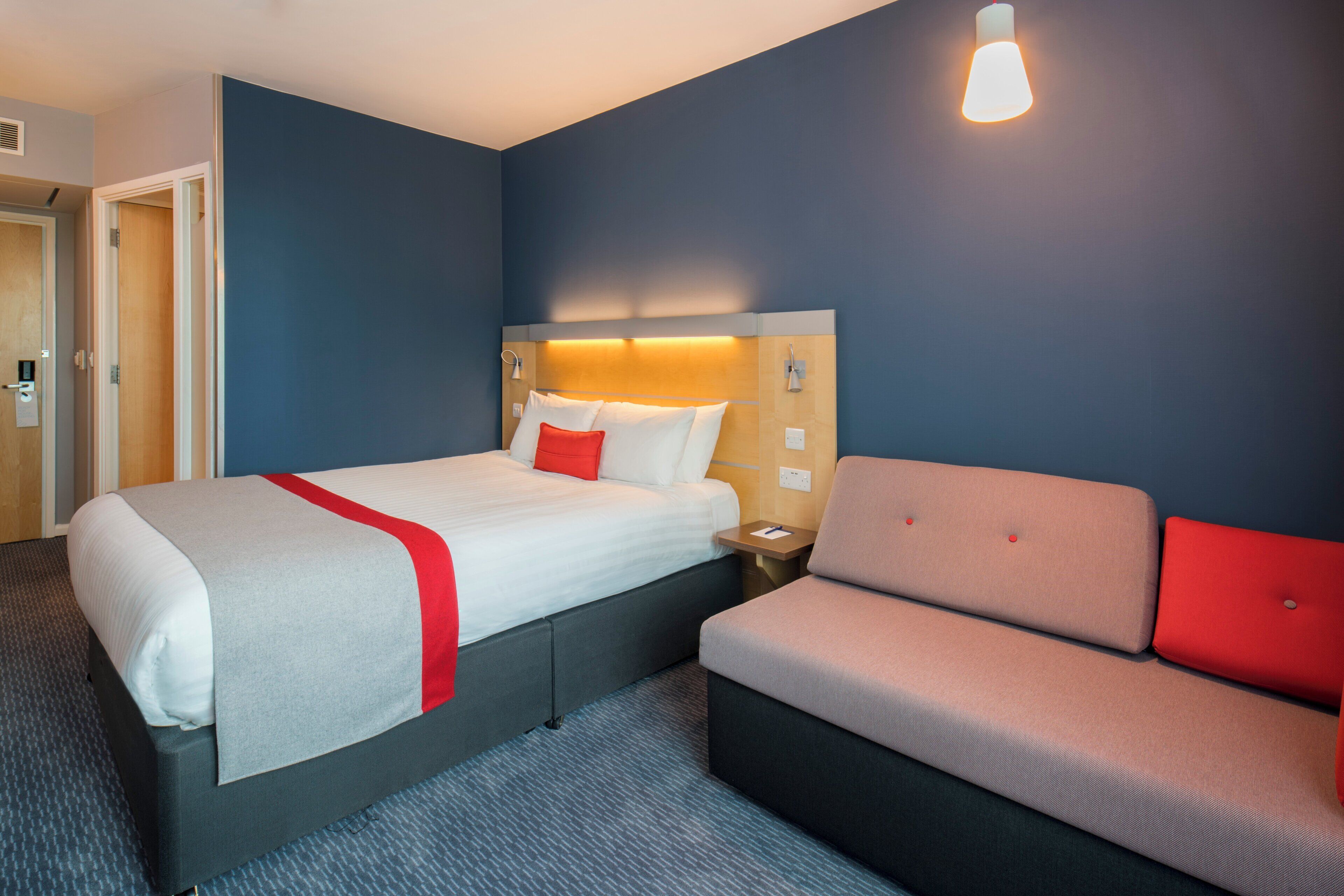 A hotel room with a bed, bedside table, and a sofa.