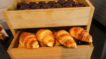 A wooden display case with three compartments containing chocolate cookies, croissants, and muffins.