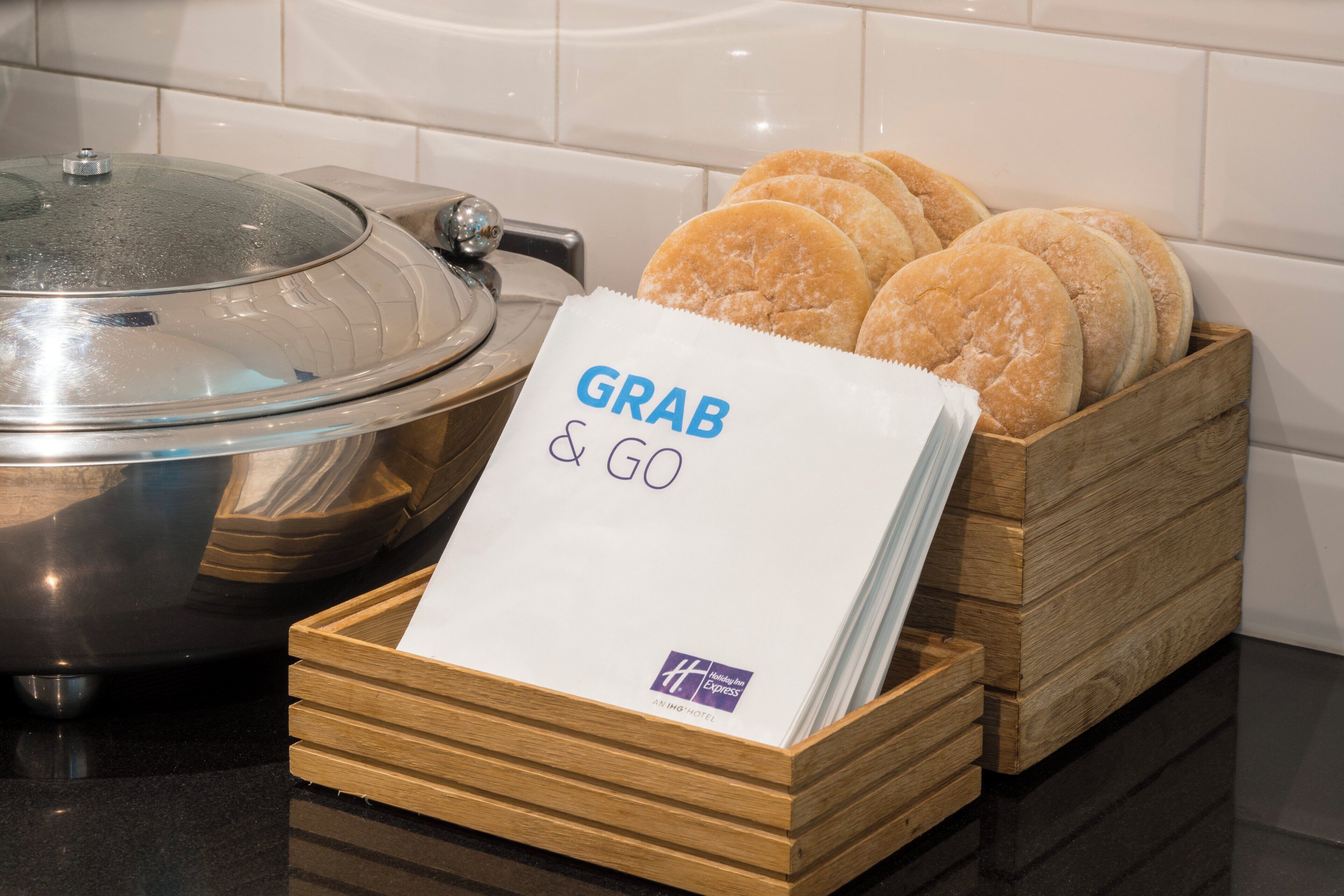 A kitchen counter with a wooden bread box containing several loaves of bread and a paper towel with 'GRAB & GO' written on it.