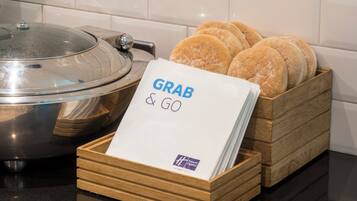 A kitchen counter with a wooden bread box containing several loaves of bread and a paper towel with 'GRAB & GO' written on it.