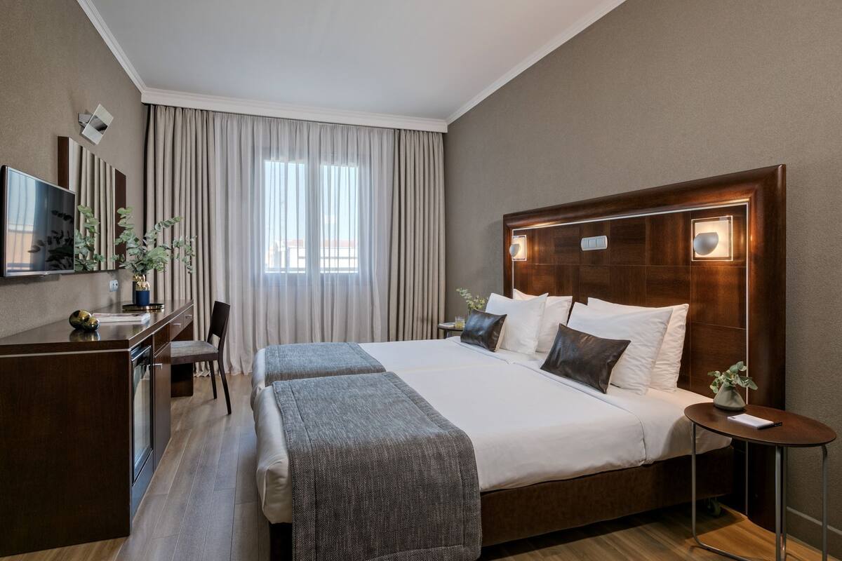 A hotel room with a large bed, a desk with a chair, a small table, and a mirror.
