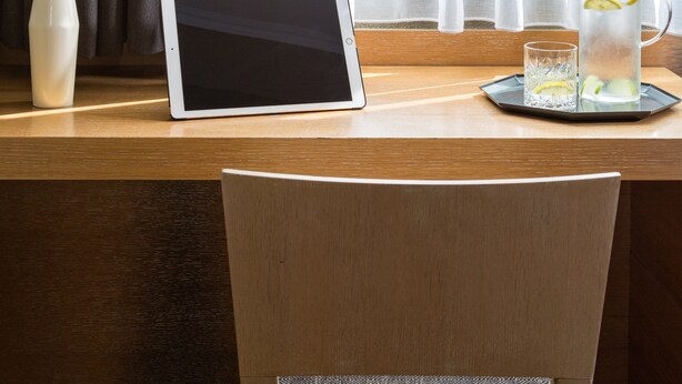 Un bureau en bois, une tablette, un verre d’eau avec des rondelles de citron et une grande plante verte.