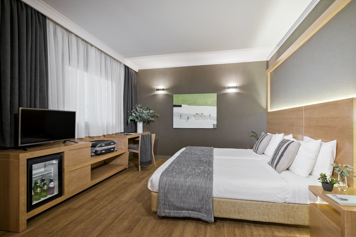 A modern hotel room with a bed, a TV, a mini-fridge, and a desk.