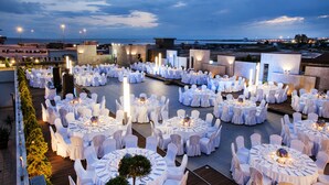 Un espace événementiel situé sur un toit, avec plusieurs tables rondes disposées pour les repas, entourées de chaises blanches, sous un ciel nocturne.