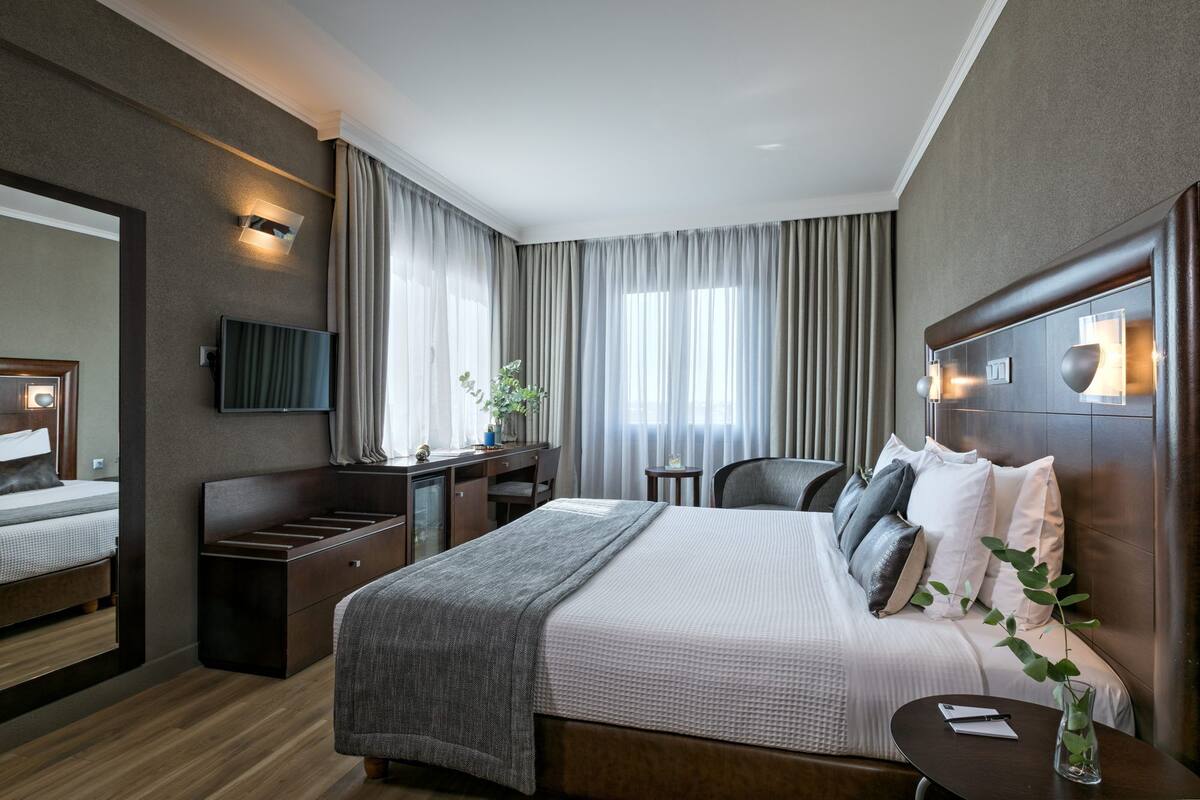 A modern hotel room with a large bed, a desk, a chair, a TV, and a window with curtains.