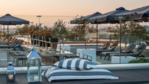 Un espace aménagé au bord de la piscine, avec des chaises longues, des parasols et une vue dégagée sur le paysage urbain en arrière-plan.
