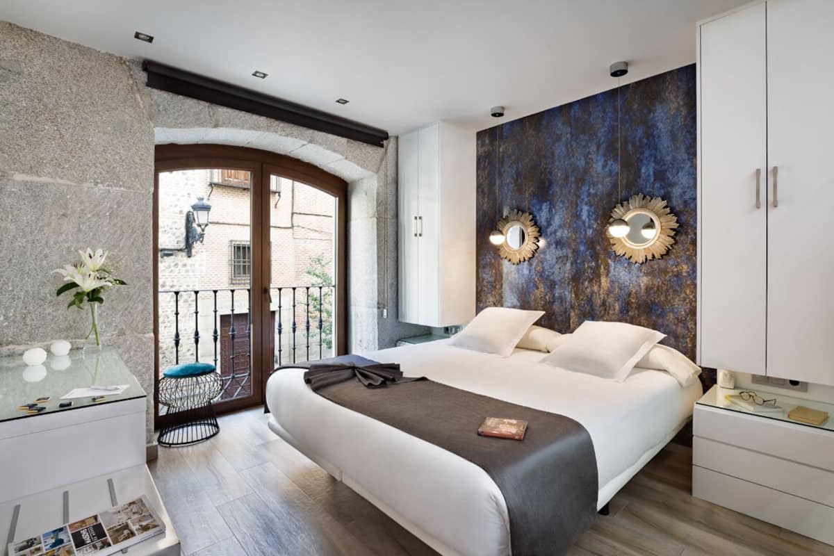 A modern bedroom with a large bed, a glass desk, and a view of the outside.