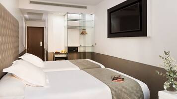 A hotel room with a large bed, a bedside table with toiletries, a glass cabinet, and a TV mounted on the wall.