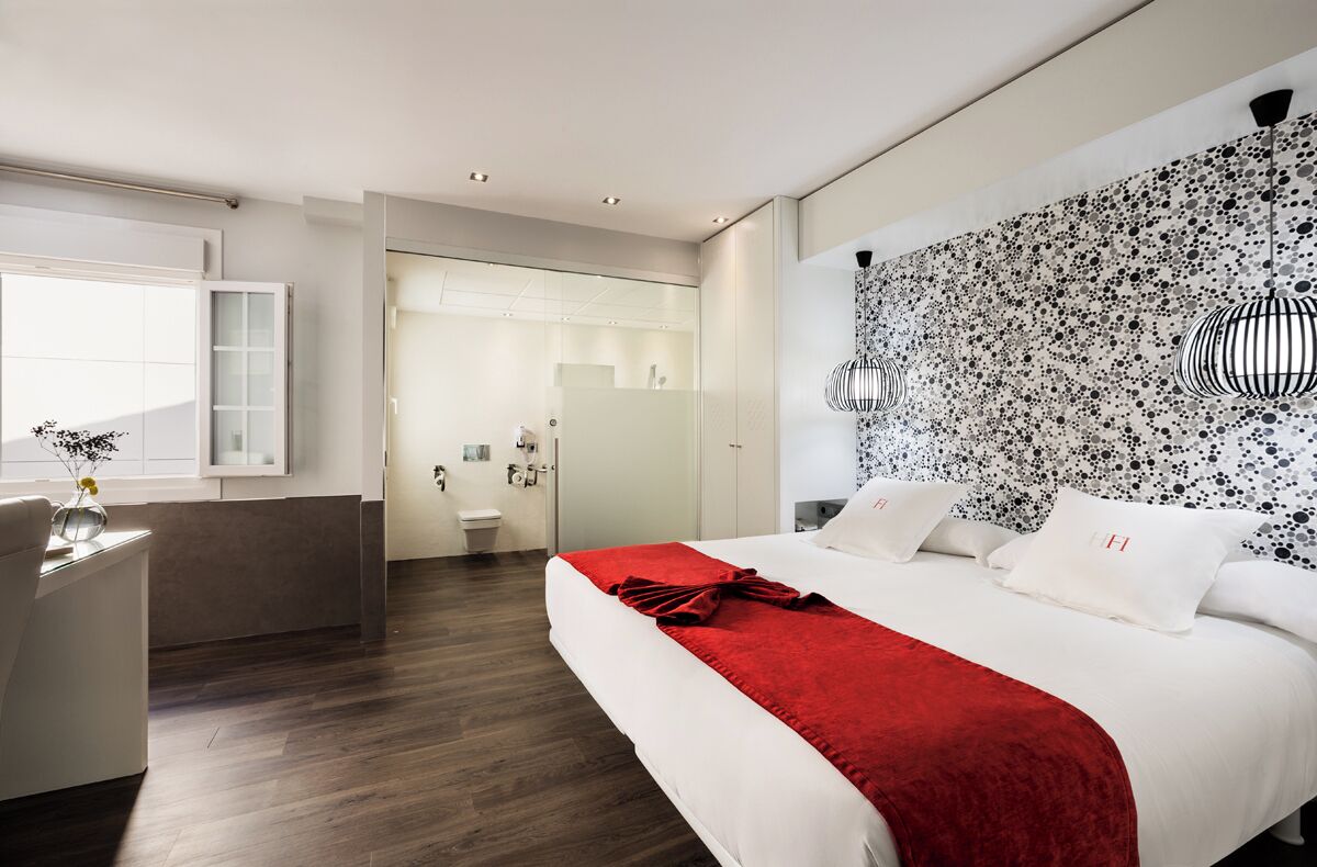 Habitació d'hotel moderna amb un llit gran, un escriptori i un bany visible a través d'una porta oberta.