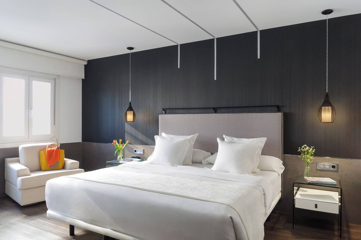 A modern hotel room with a large bed, bedside tables, a chair, and a window.