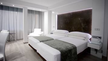 Una habitación de hotel moderna con dos camas, una zona de estar con una silla, un escritorio y un amplio ventanal con cortinas.