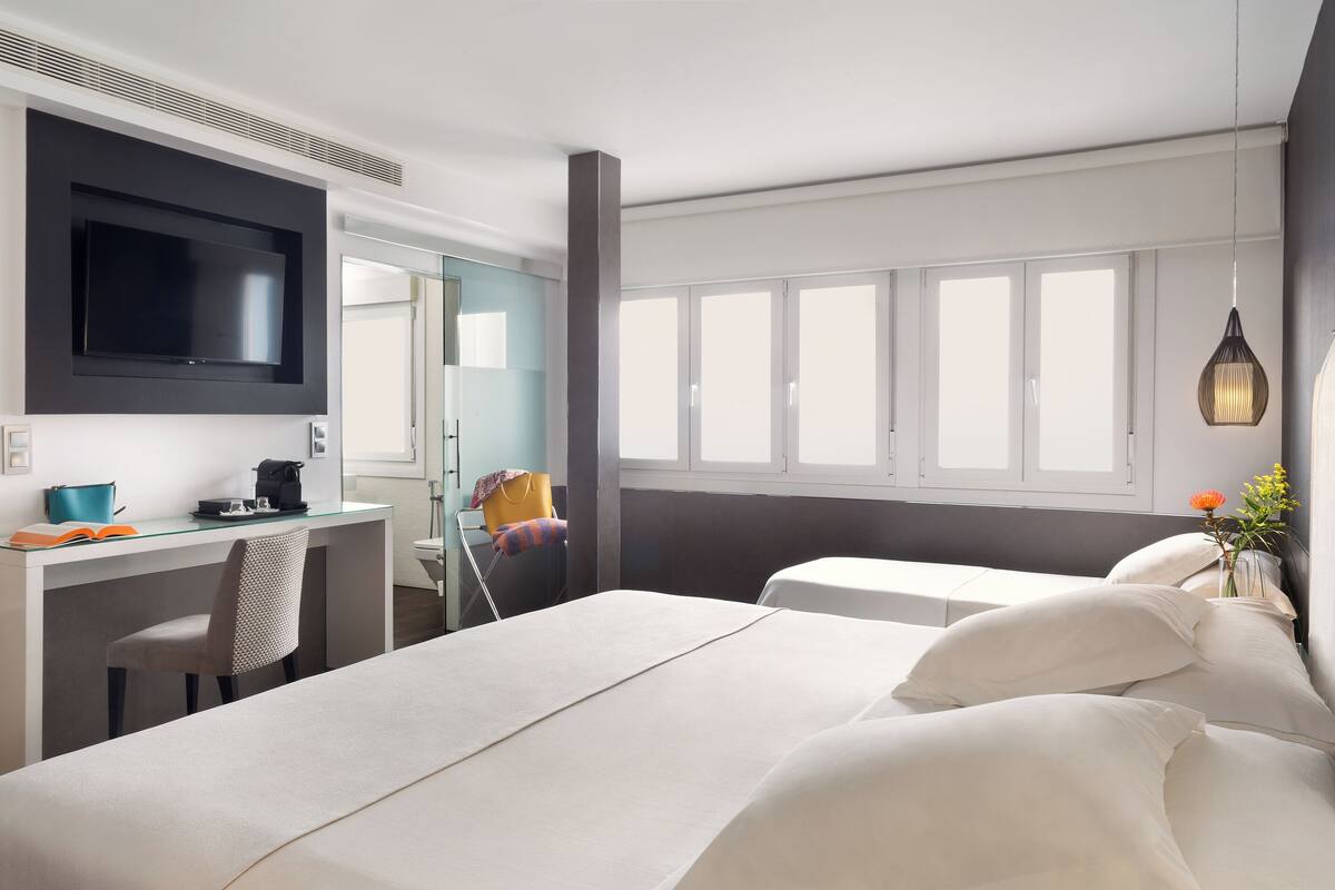 A modern hotel room with a large bed, a desk with a flat-screen TV, and a window with multiple panes.