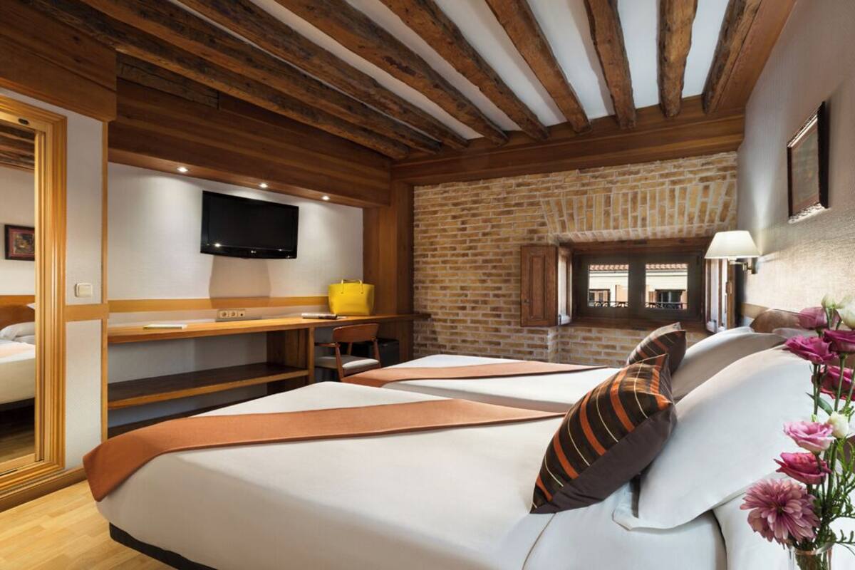 Ein Hotelzimmer mit Holzbalken, einer Ziegelwand, einem Fernseher, einem Bett, einem Schreibtisch und einem Stuhl.