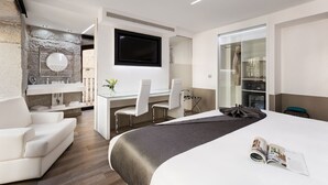A modern hotel room with a large bed, a desk with two chairs, a TV, and a bathroom with a stone wall. - Hotel Francisco I (Madrid)