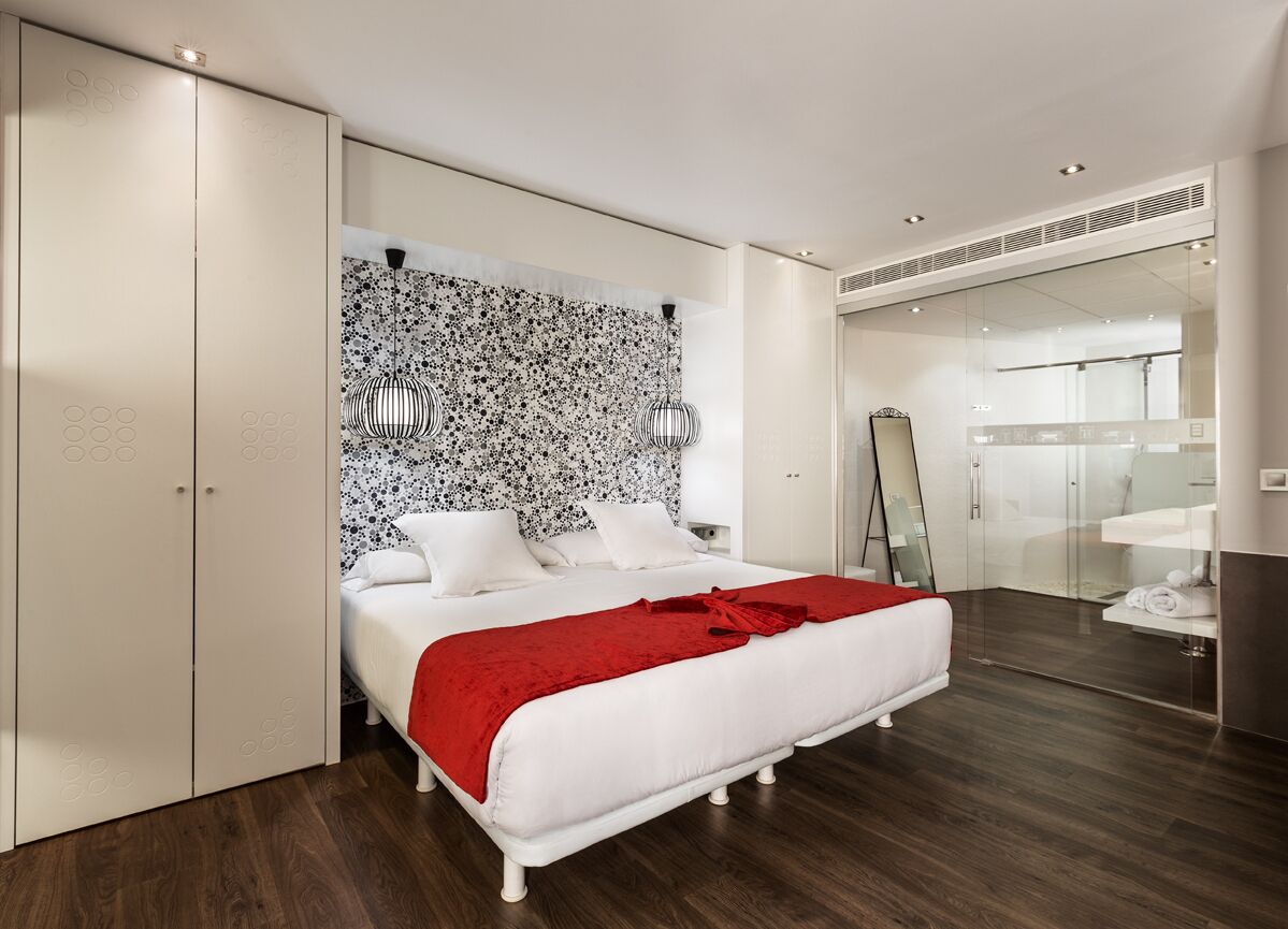 Un dormitorio moderno con una cama grande, una manta roja, un cabecero estampado y una mampara de ducha de vidrio.