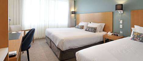 A hotel room with two beds, a desk, a chair, a lamp, a phone, and a nightstand.