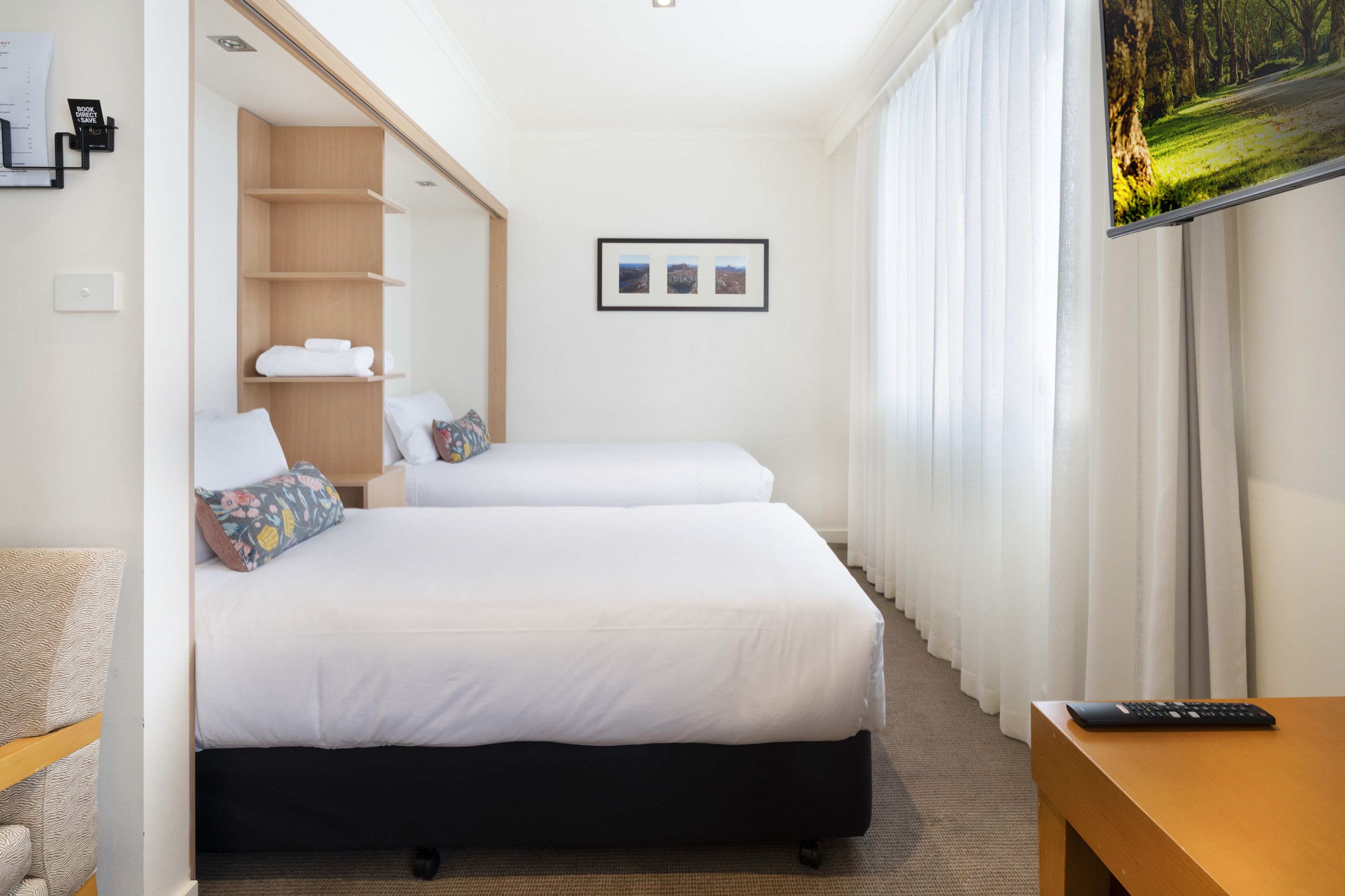 A hotel room with two beds, a wooden desk, a TV, and a framed picture on the wall.