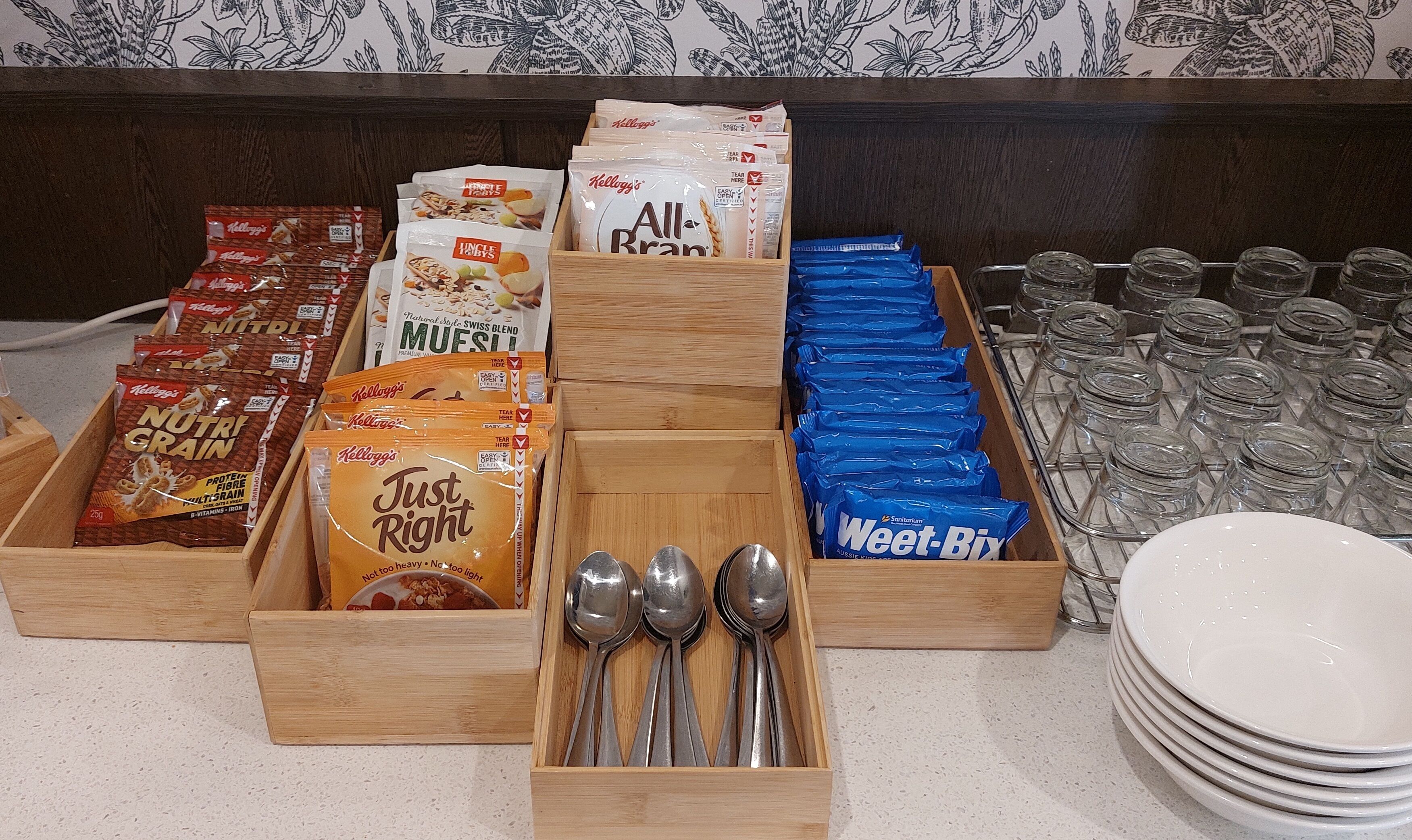 A breakfast buffet with various cereal options, utensils, and glassware.