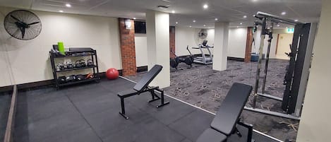 Un gimnasio con bancos de pesas, una cinta de correr y un ventilador de pared.
