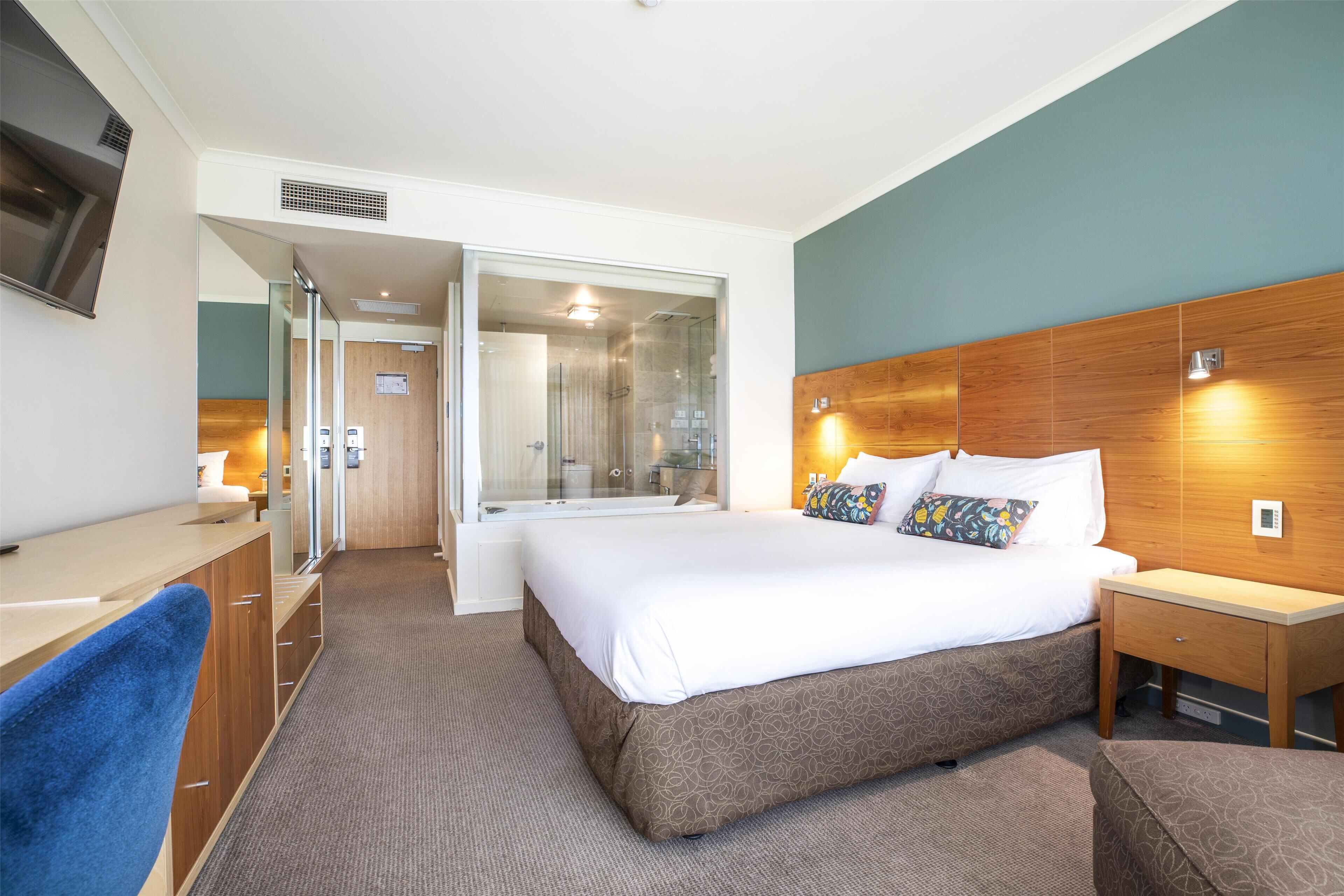 A modern hotel room with a large bed, a desk, and a shower area.