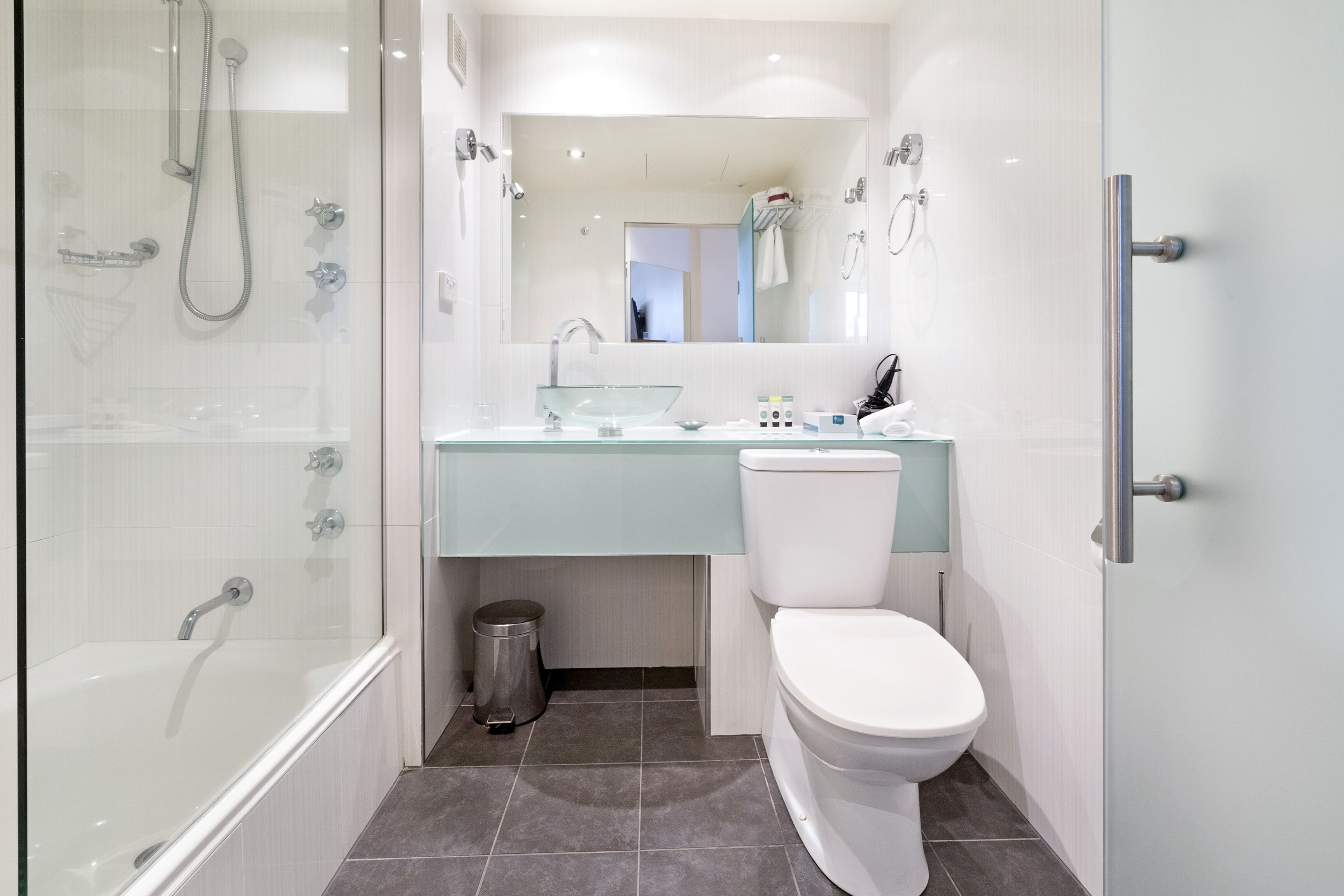 Une salle de bain moderne avec une douche à parois de verre, un lavabo en verre et des toilettes blanches.
