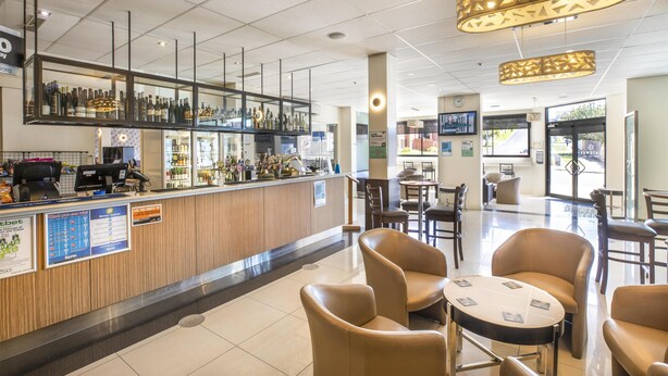 A bar area with a wooden counter, various bottles, and a seating area with leather chairs and tables. - Nightelier Devonport Gateway Hotel  (Devonport)