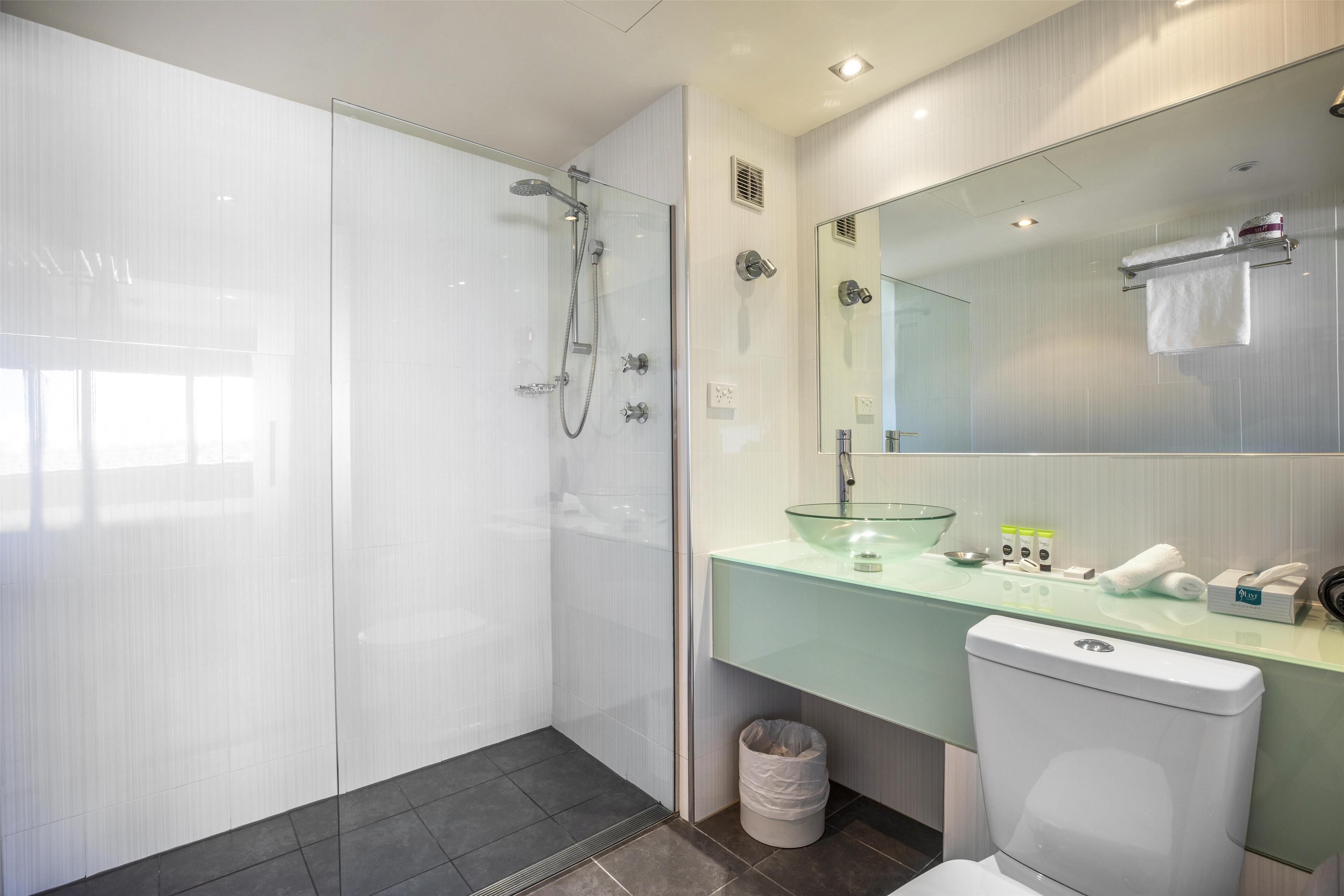 A modern bathroom with a glass shower enclosure, a glass sink, and a toilet.